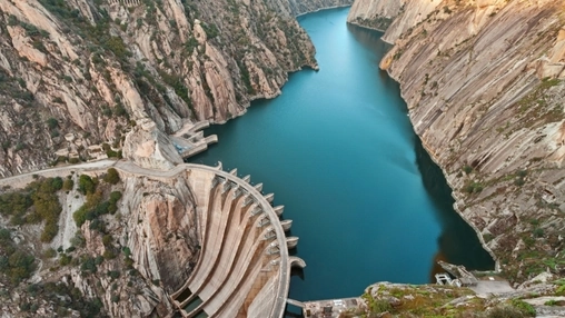 Aerial view of a large dam and reservoir set between rocky cliffs